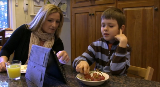 母亲儿童厨房桌吃葡萄和谈话使用ipad